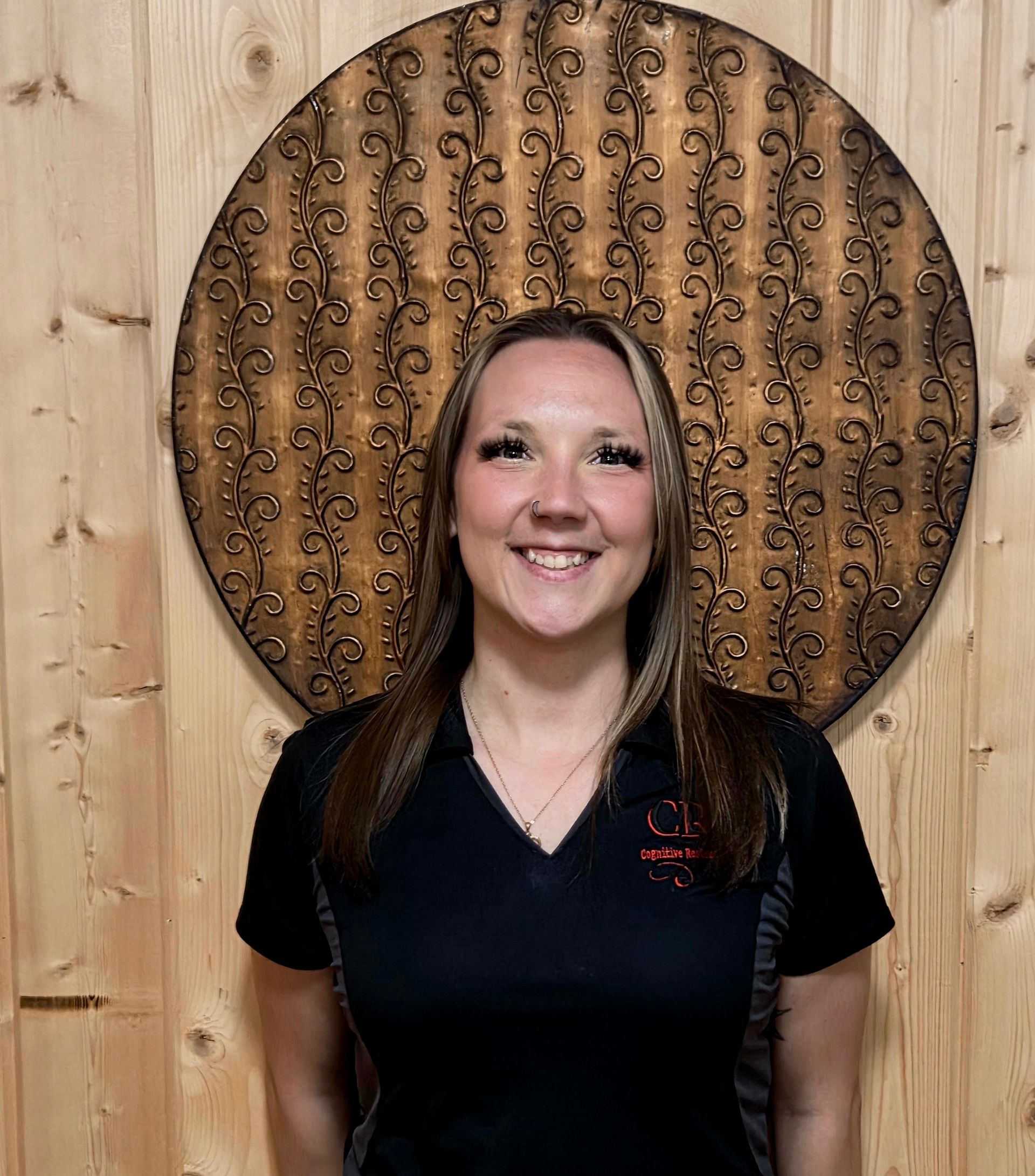 A woman in a black shirt is standing in front of a wooden wall.