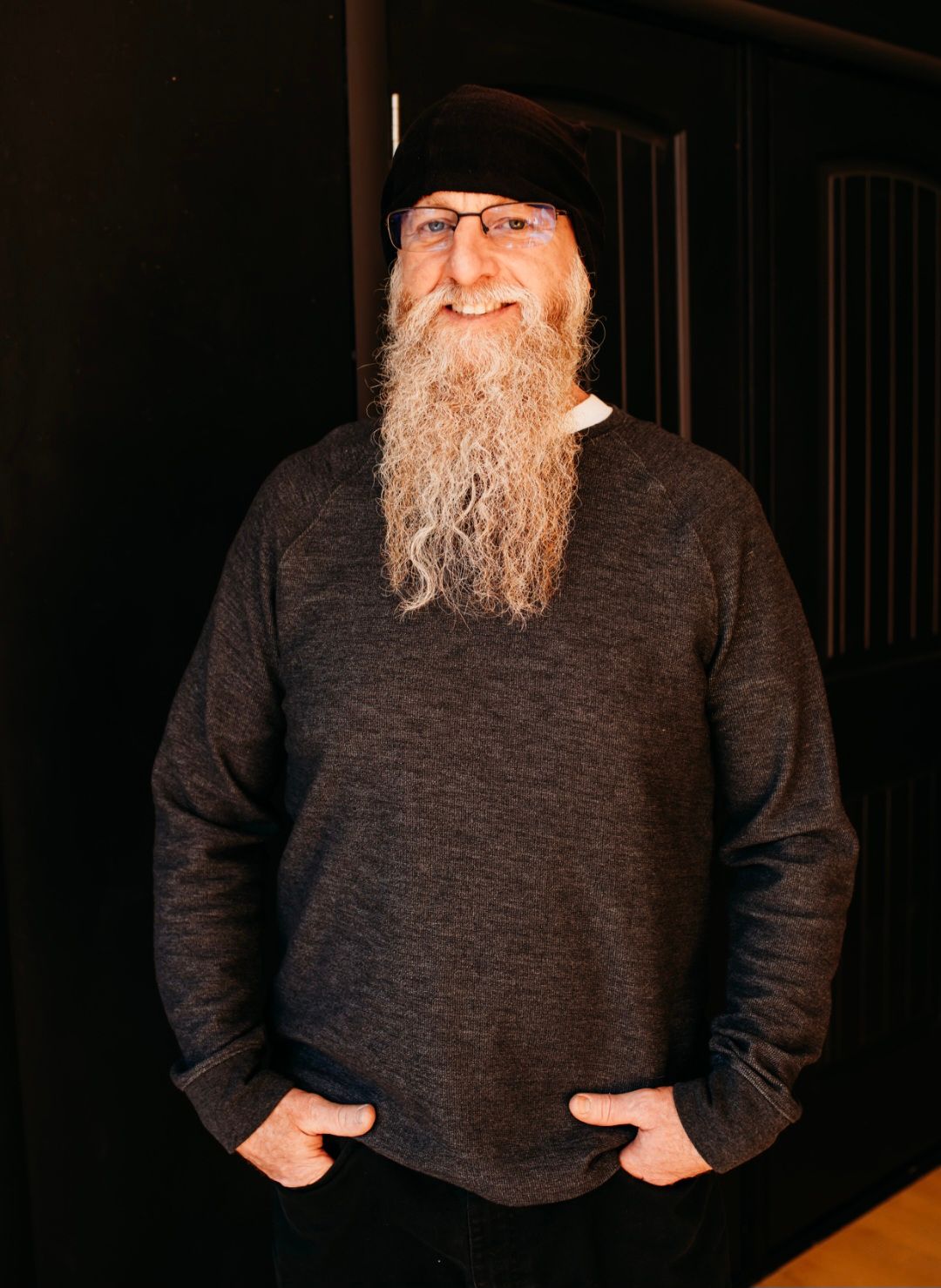 A man with a beard and glasses is wearing a sweater and a hat.