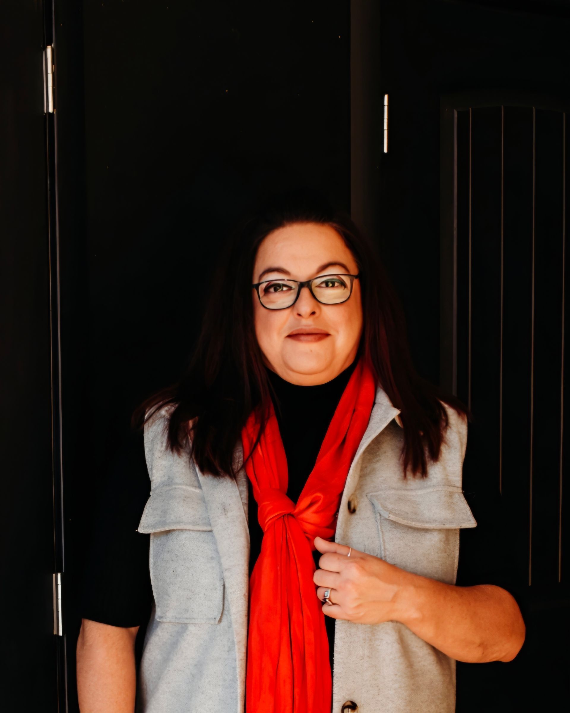 A woman wearing glasses and a red scarf is standing in front of a door.