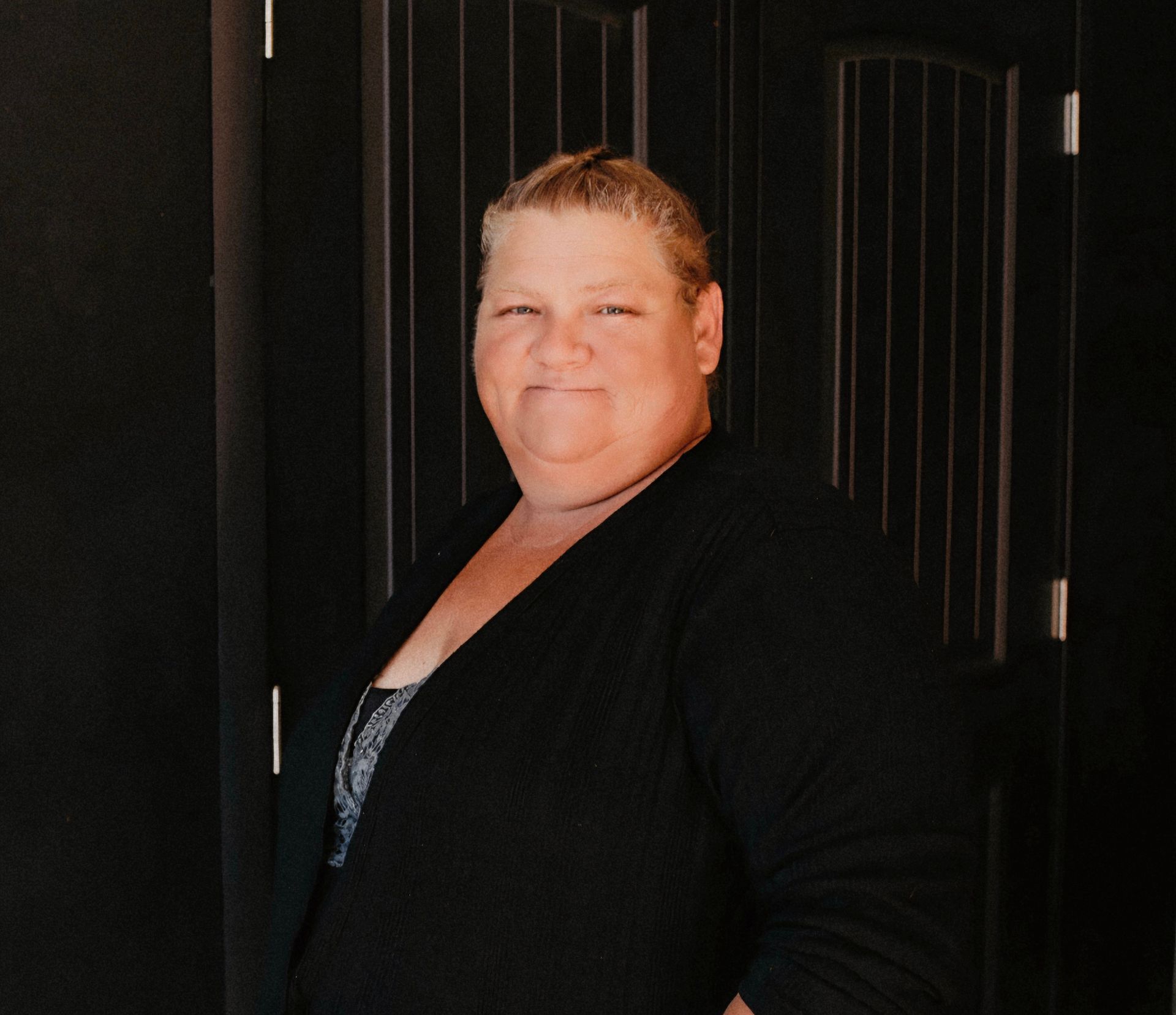 A woman in a black sweater is standing in front of a black door