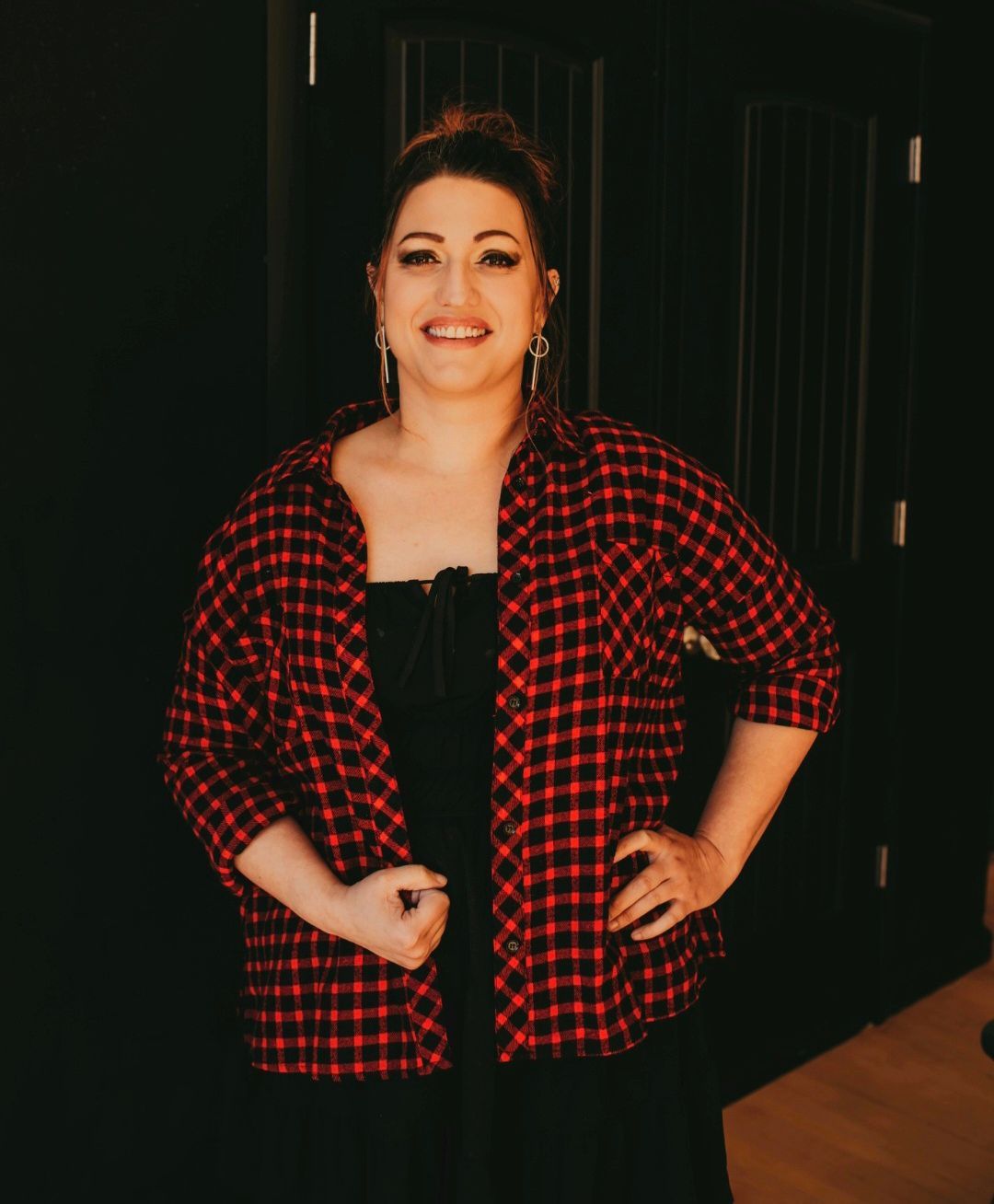 A woman is wearing a red plaid shirt and a black dress.