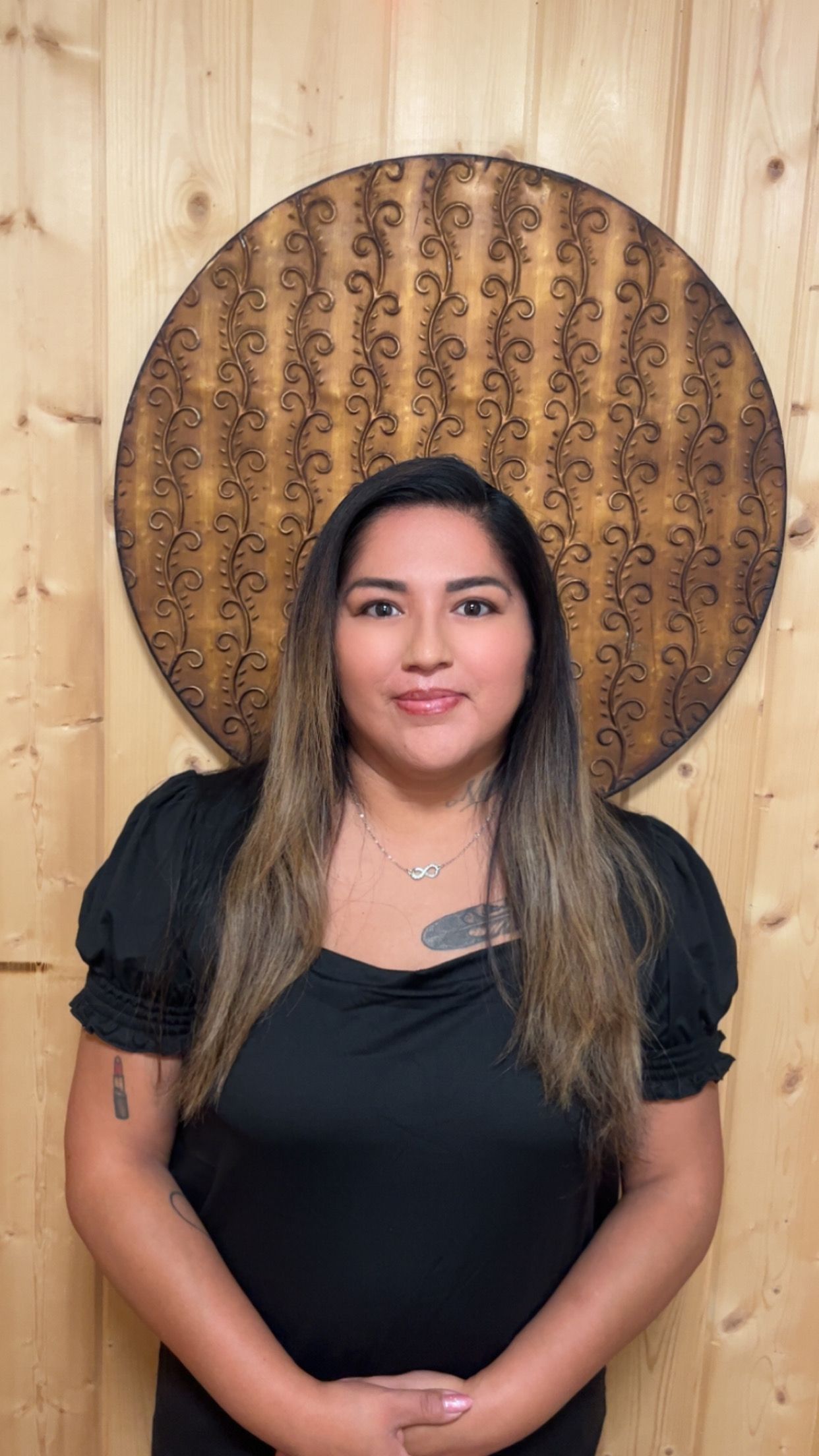 A woman in a black shirt is standing in front of a wooden wall.