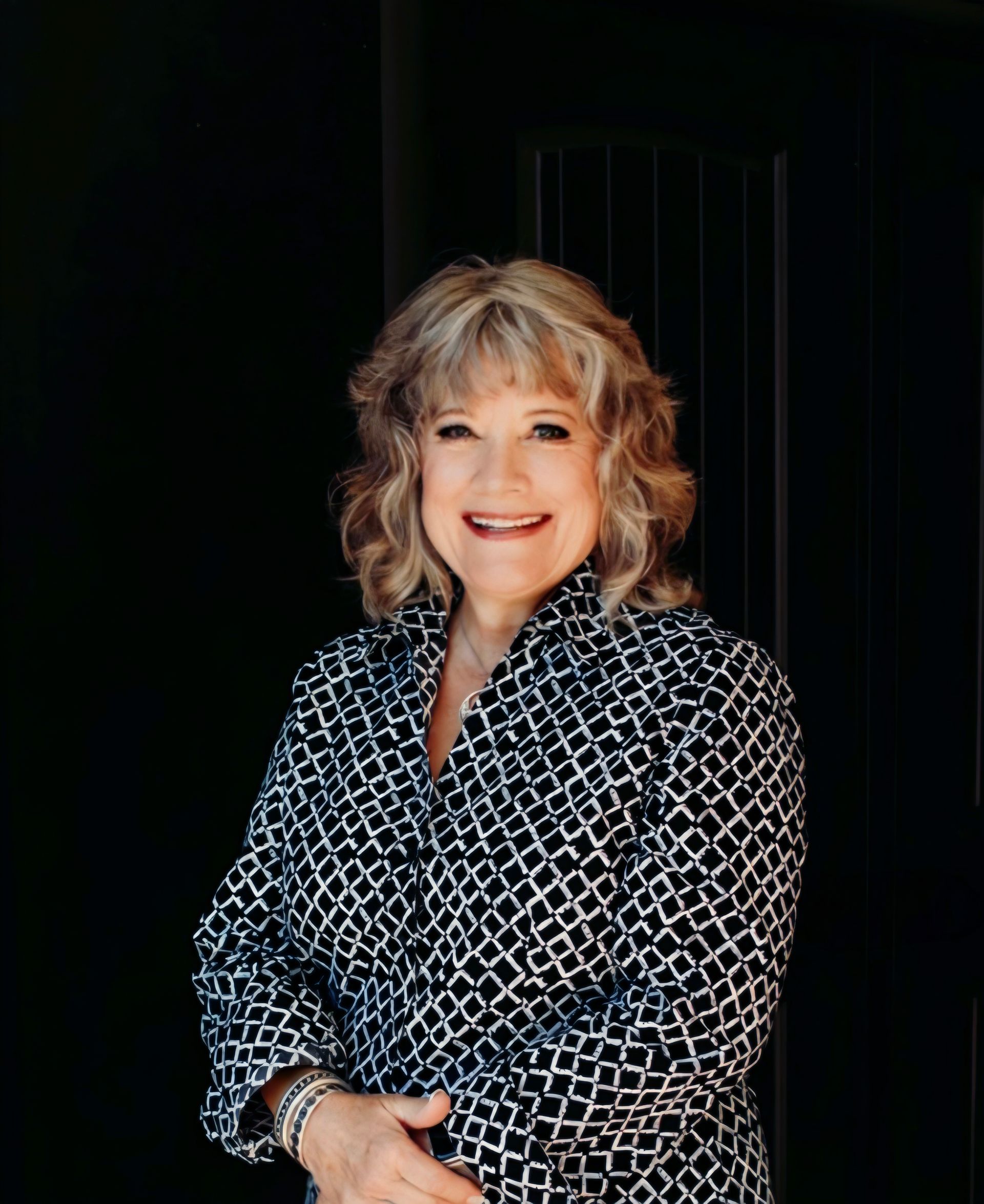 A woman in a black and white shirt is standing in front of a black door.