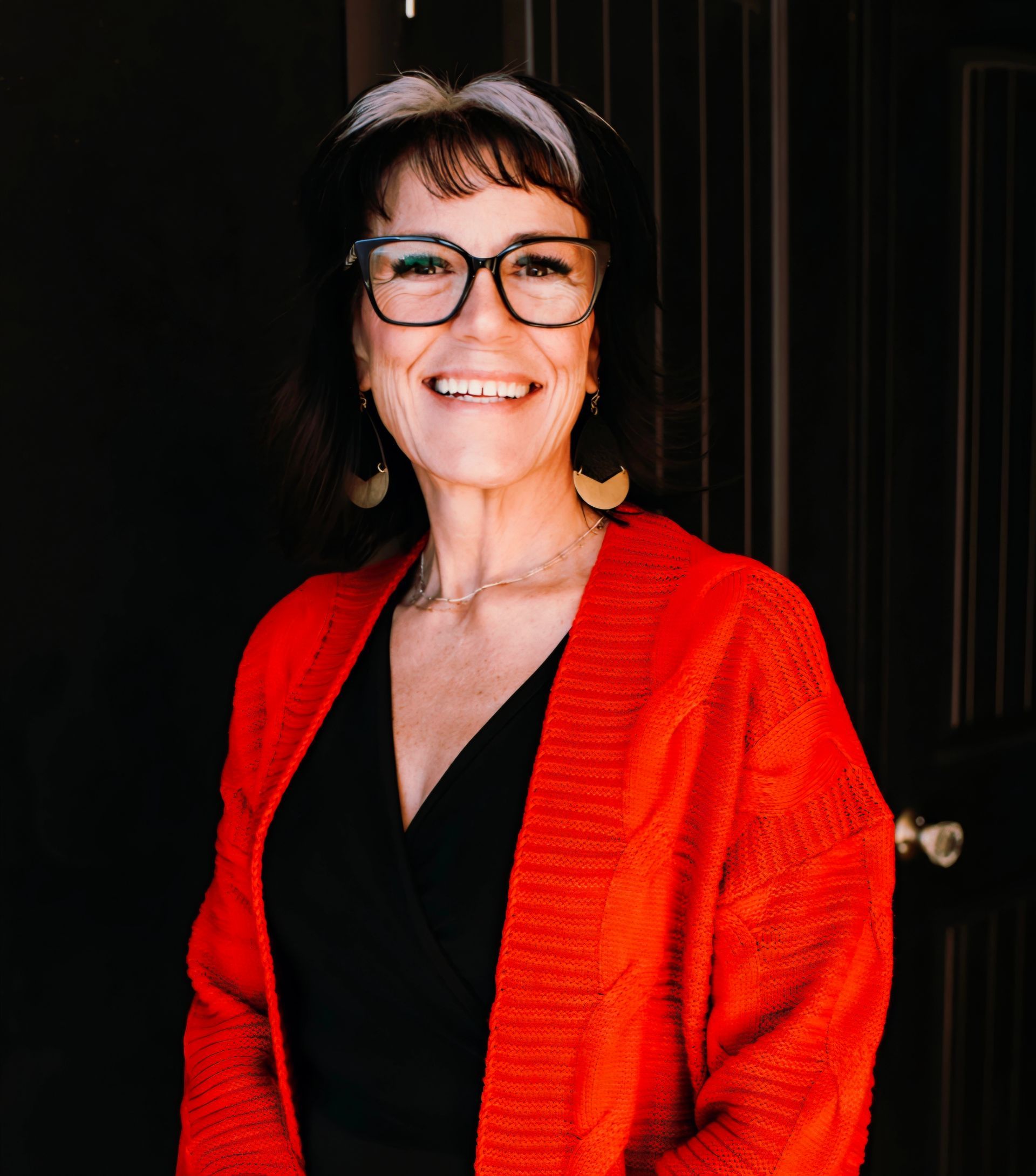 A woman wearing glasses and a red sweater is standing in front of a door.
