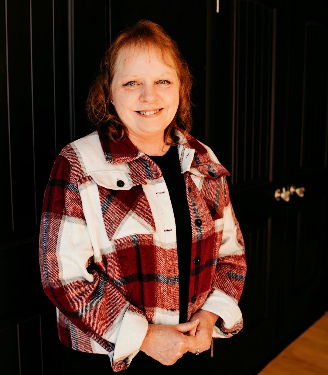 A woman in a plaid jacket is standing in front of a black door.