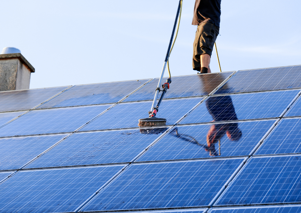 A man is cleaning solar panels on a roof with a broom.