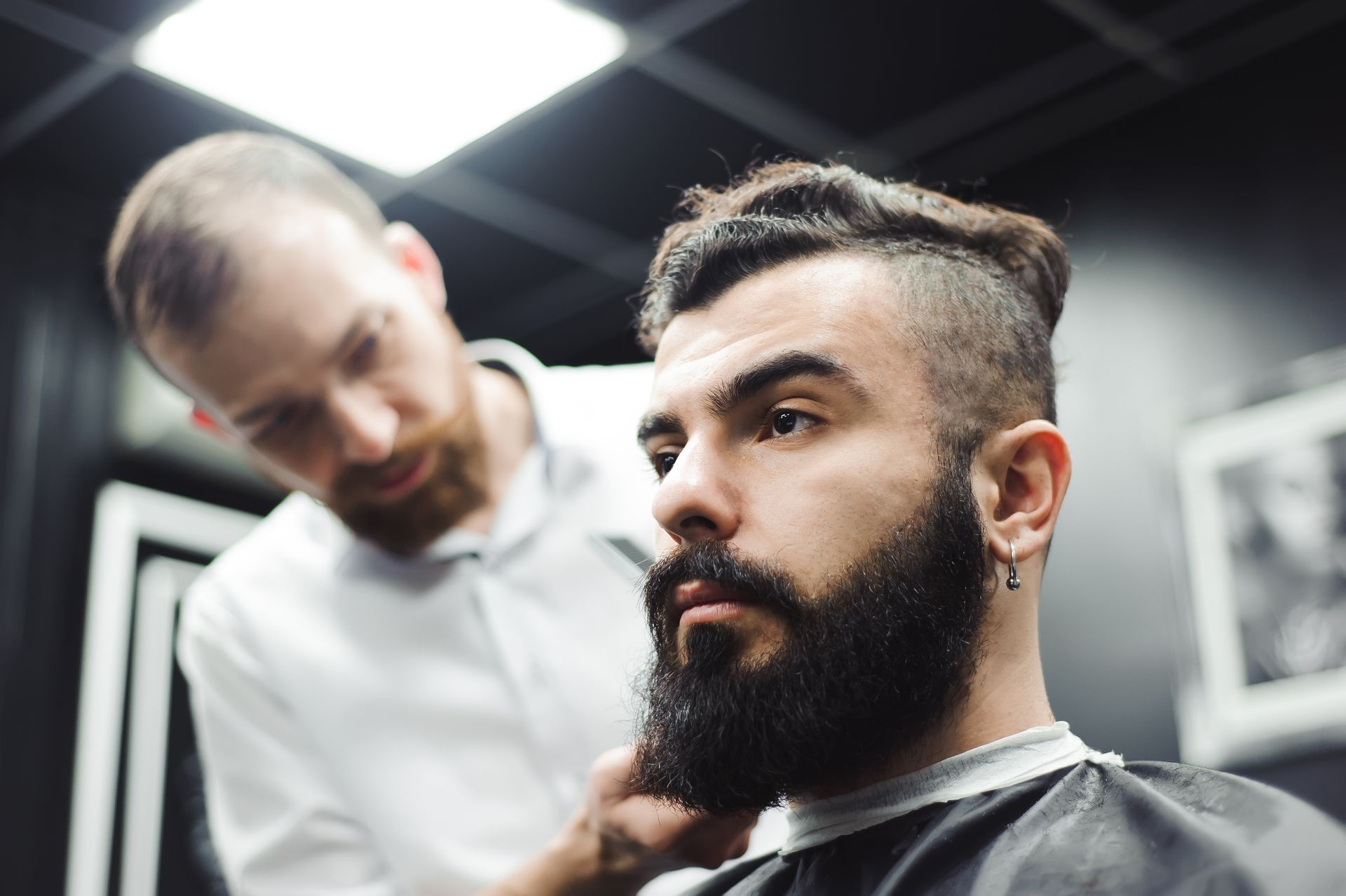 A man with a beard is getting his hair cut by a barber in a barber shop.