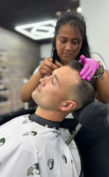 A man is getting his hair cut by a woman in a barber shop.