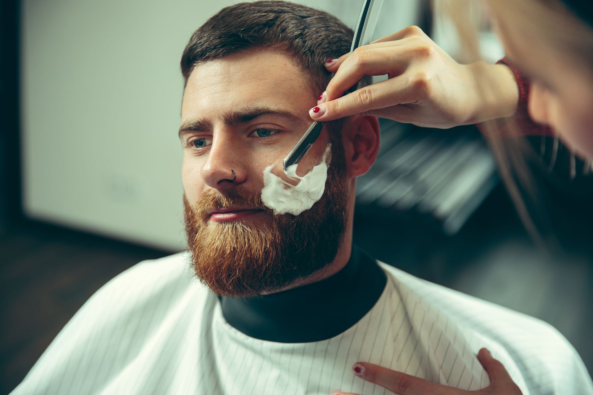 A man is getting his beard shaved at a barber shop.