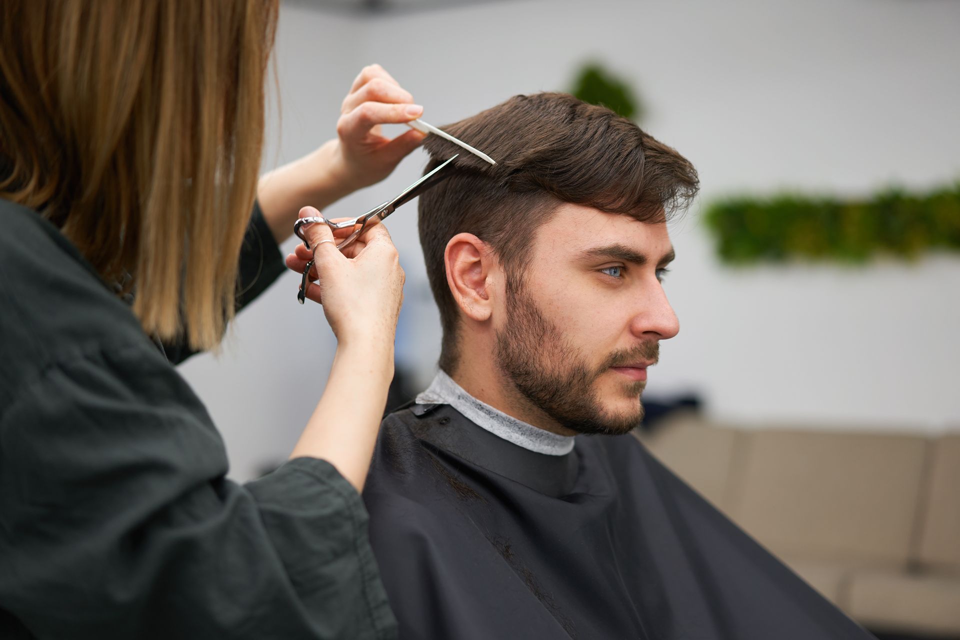 A man is getting his hair cut by a woman at a barber shop.