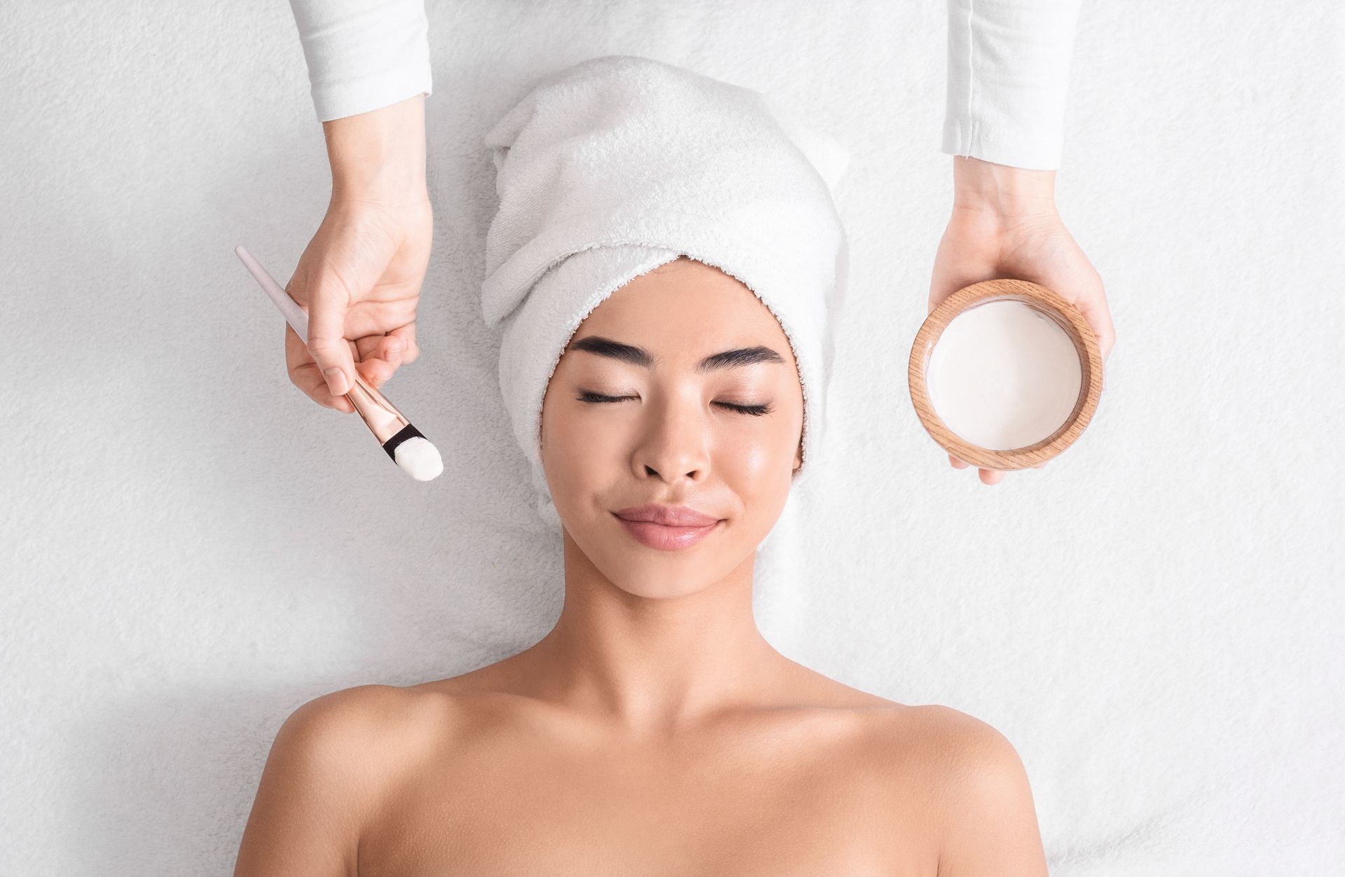 A woman with a towel wrapped around her head is getting a facial treatment at a spa.