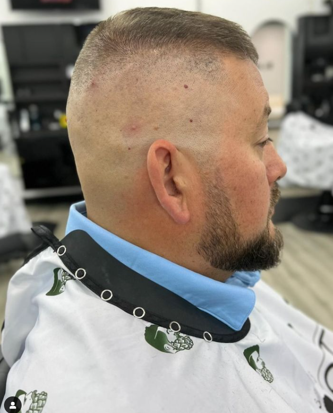 A man with a beard is getting his hair cut at a barber shop.