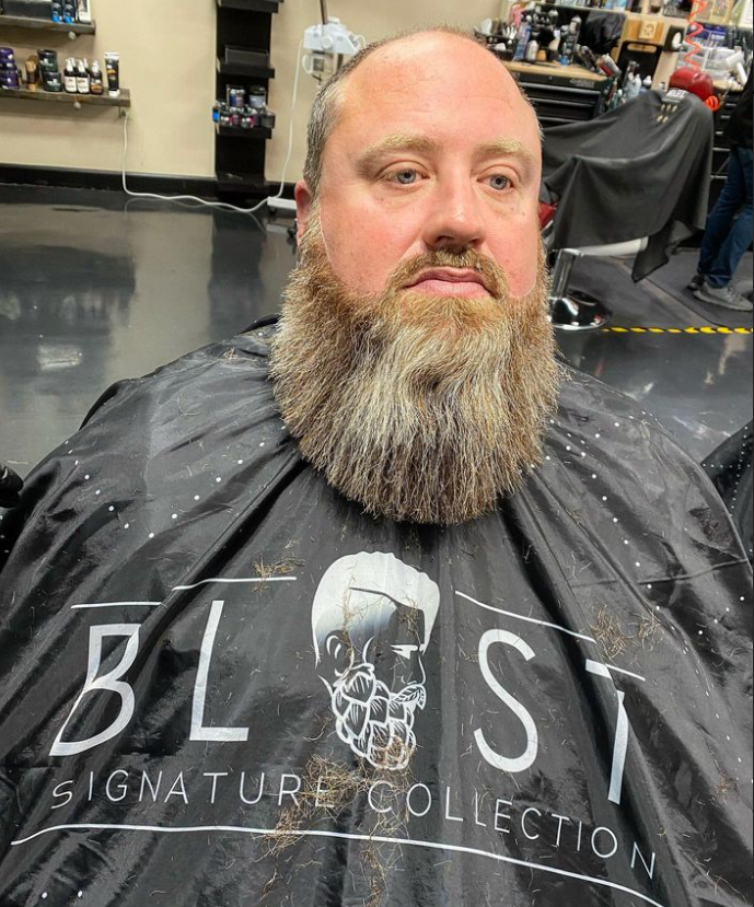 A man with a beard is getting his hair cut at a barber shop.