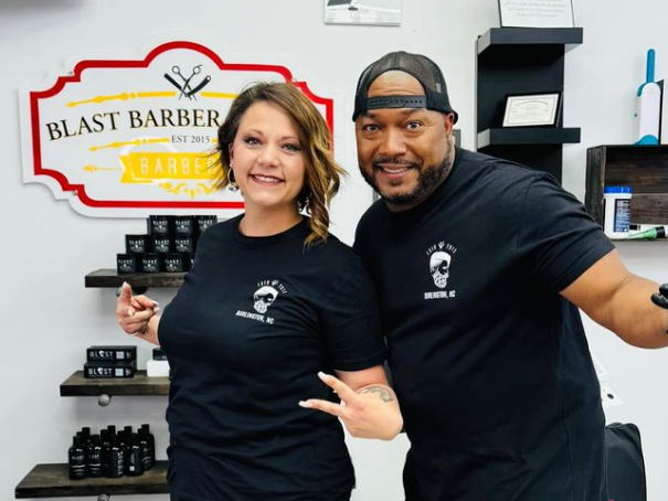 A man and a woman are posing for a picture in a barber shop.