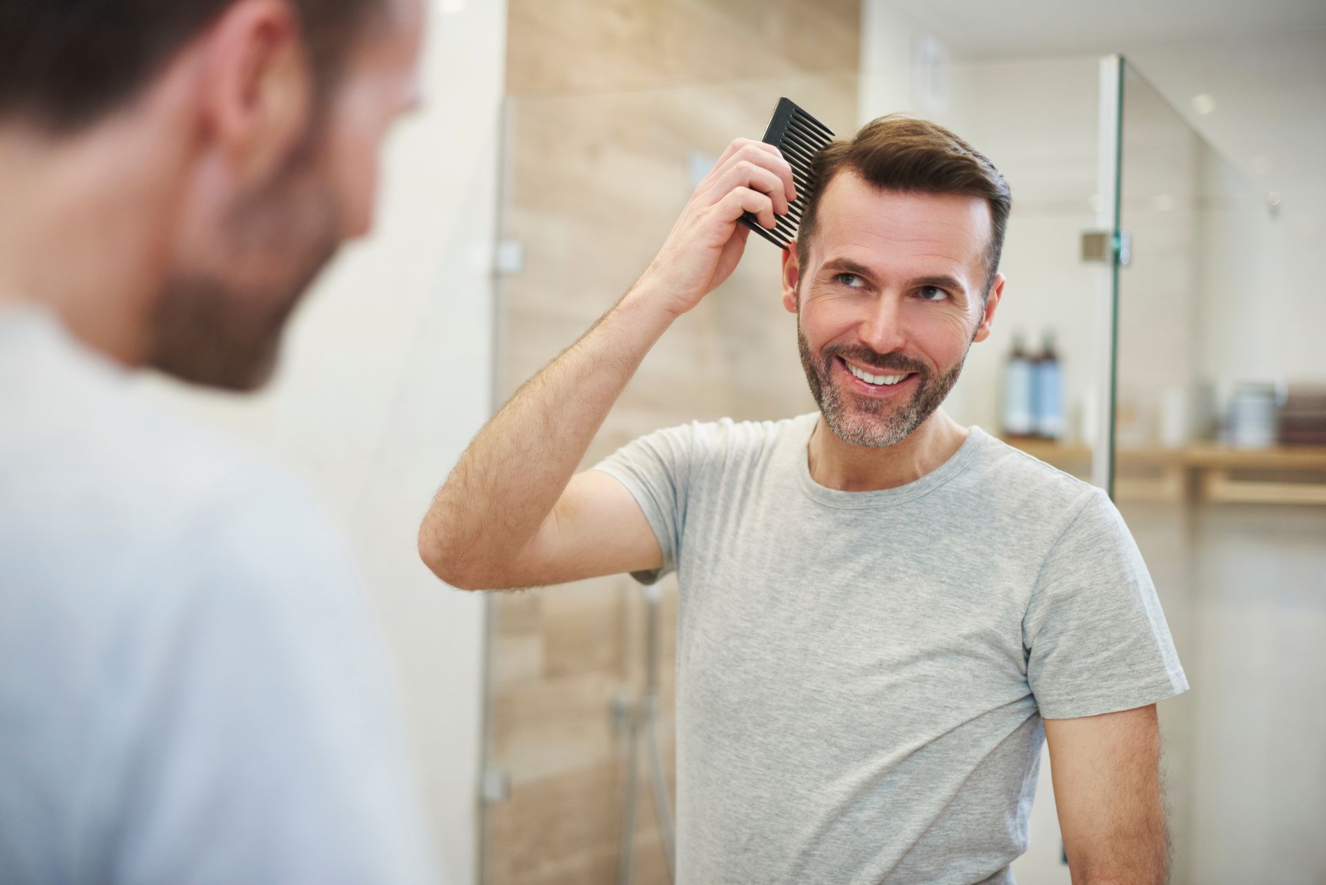 A man is brushing his hair in front of a mirror.