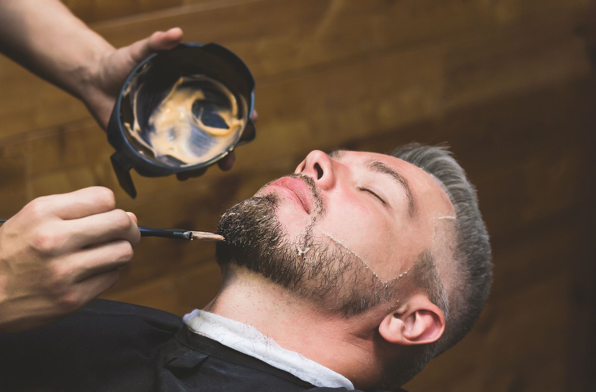 A man is getting his beard painted by a barber.