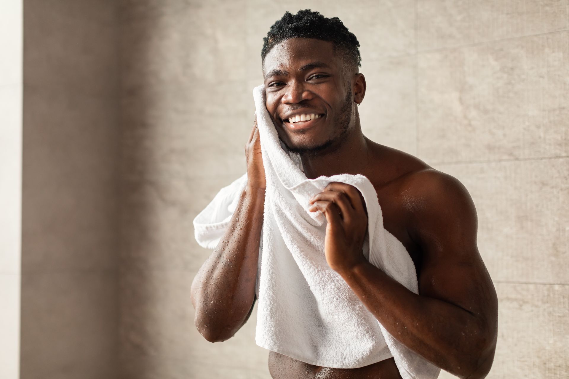 A shirtless man is wrapped in a white towel in a bathroom.