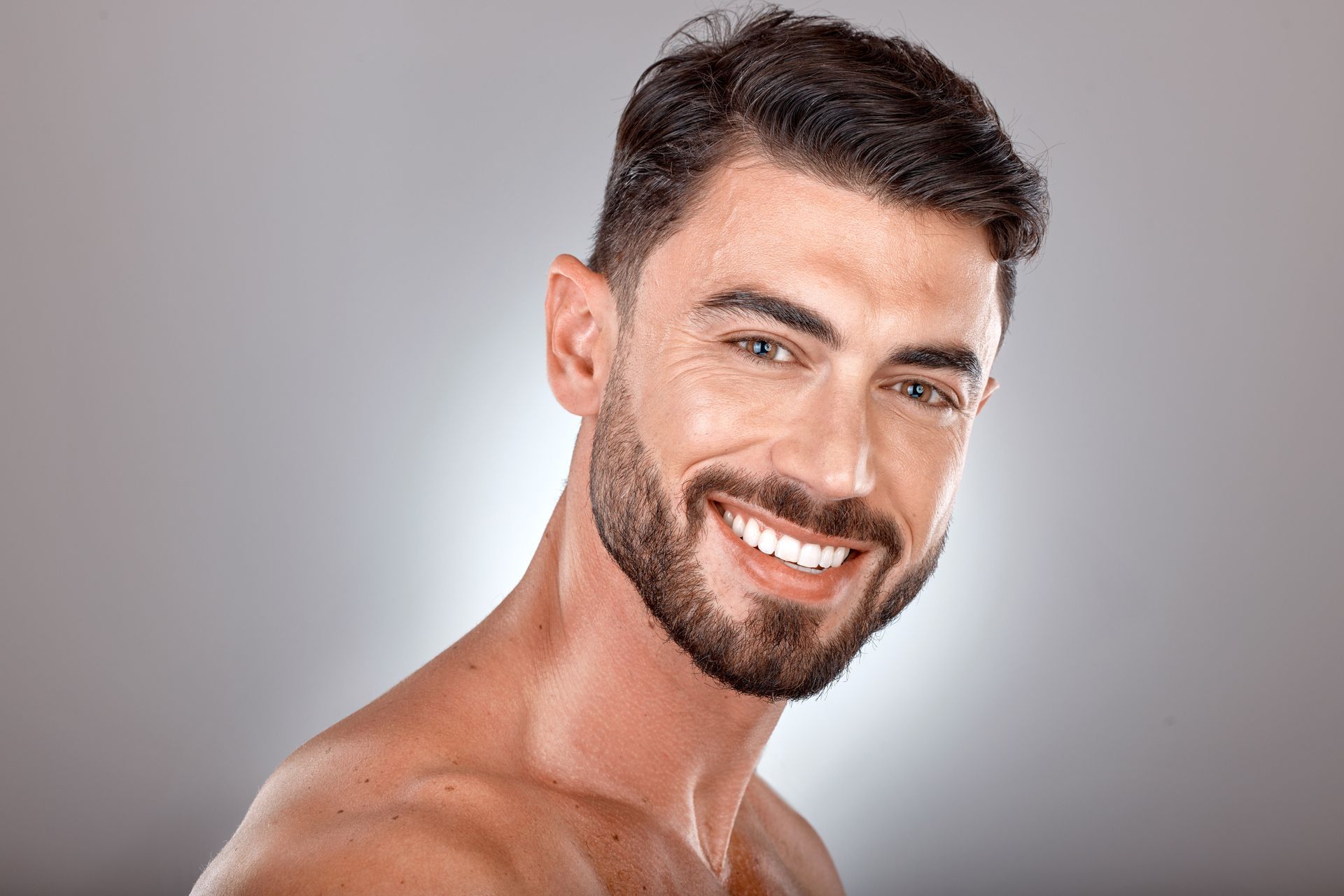 A shirtless man with a beard is smiling for the camera.