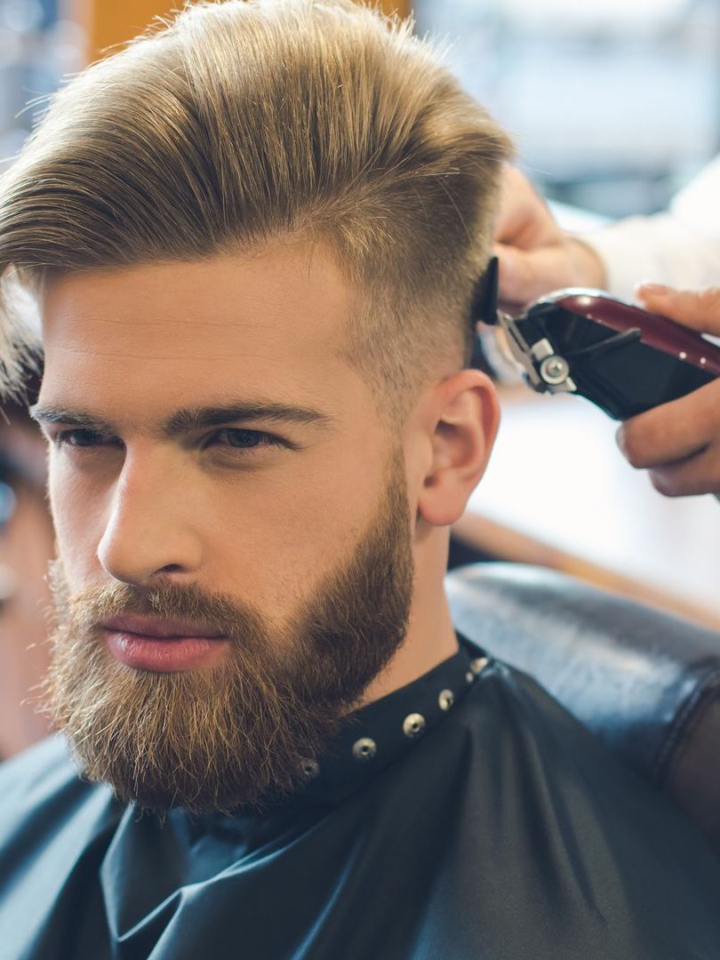 A man with a beard is getting his hair cut by a barber.