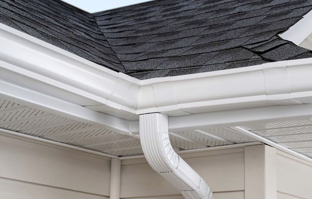 White gutters and downspout on a house with a dark gray shingle roof.