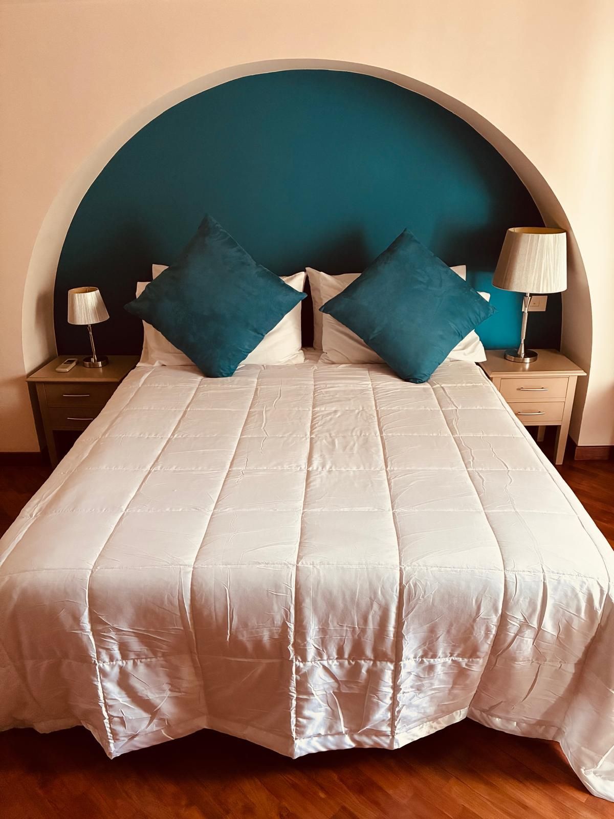 Letto con piumone bianco, cuscini color verde acqua e comodini con lampade sotto la parete ad arco color verde acqua.