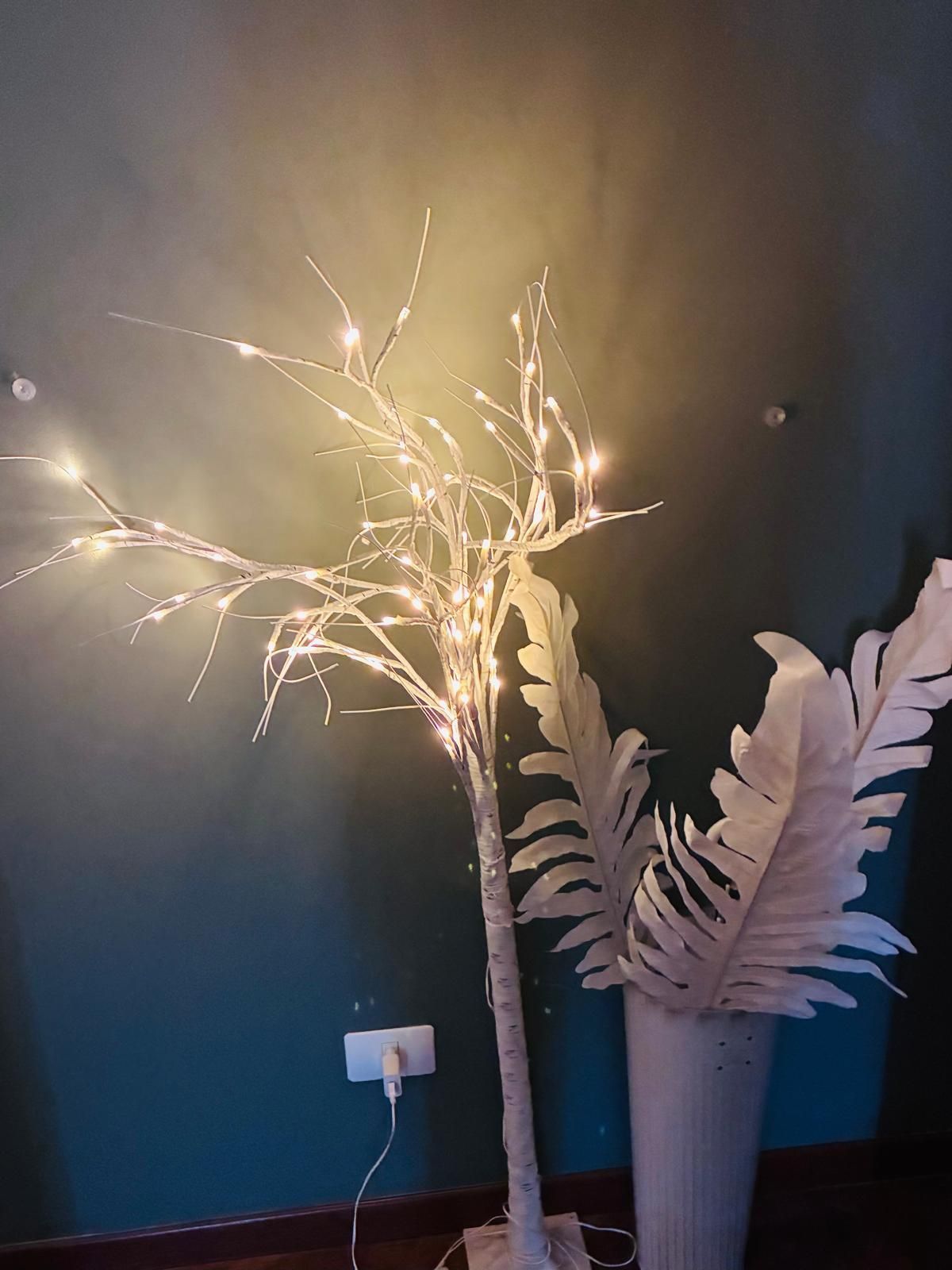 Albero artificiale illuminato con rami e foglie bianchi, contro una parete verde acqua.