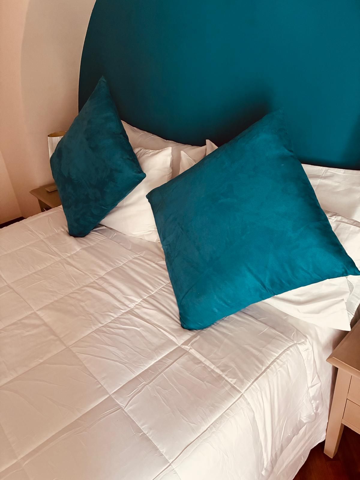 Letto con lenzuola bianche, due cuscini color verde acqua e testiera color verde acqua.