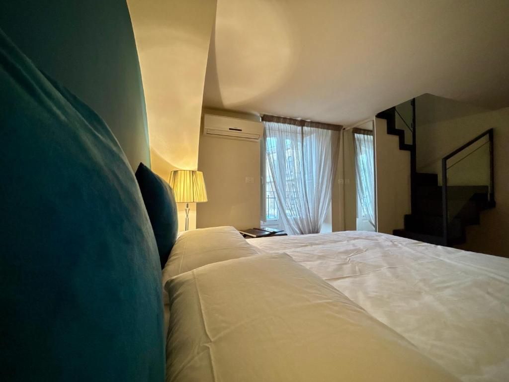 Camera da letto con letto grande, cuscini blu, lampada e scale che portano al piano superiore.