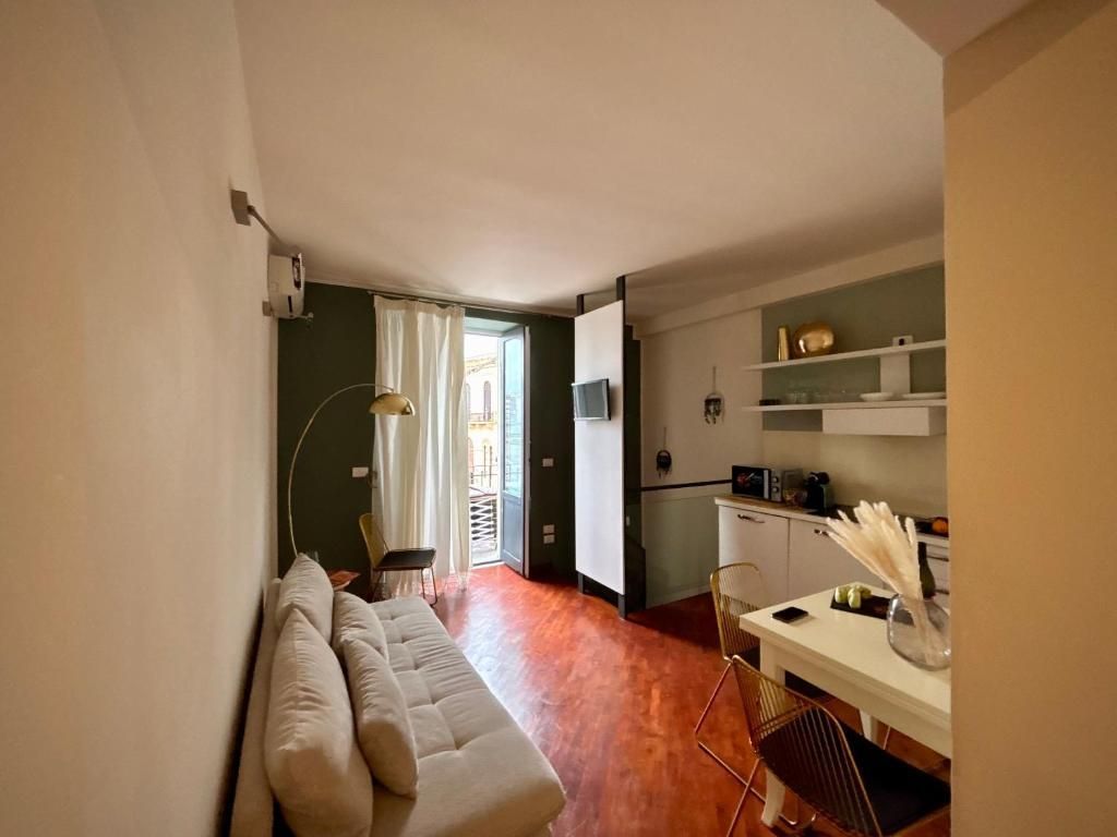 Accogliente monolocale con divano, angolo cottura e balcone. Pavimento marrone, pareti bianche e parete decorativa verde oliva.