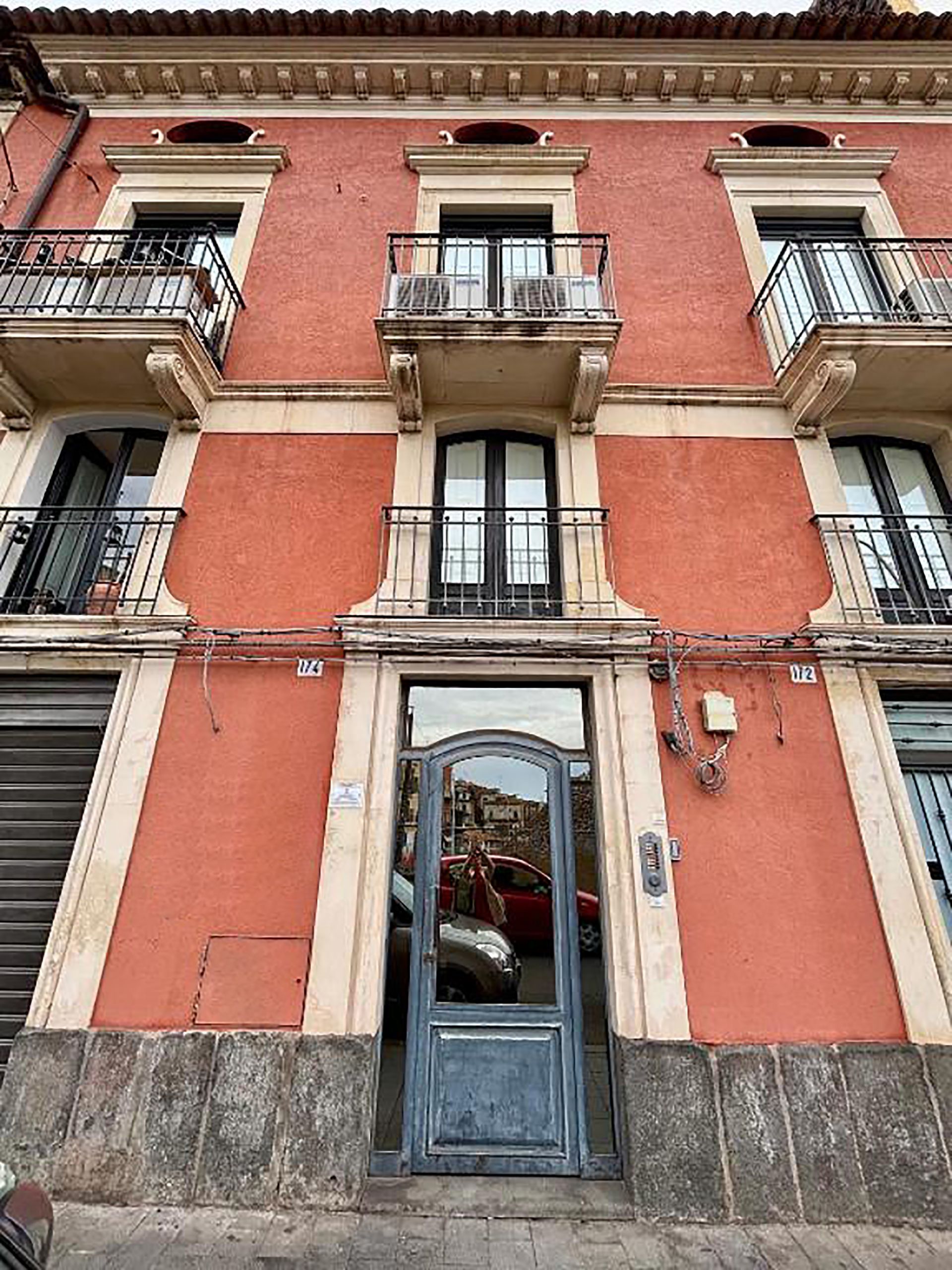 Edificio rosso con balconi, porte scure e ingresso in vetro riflettente.