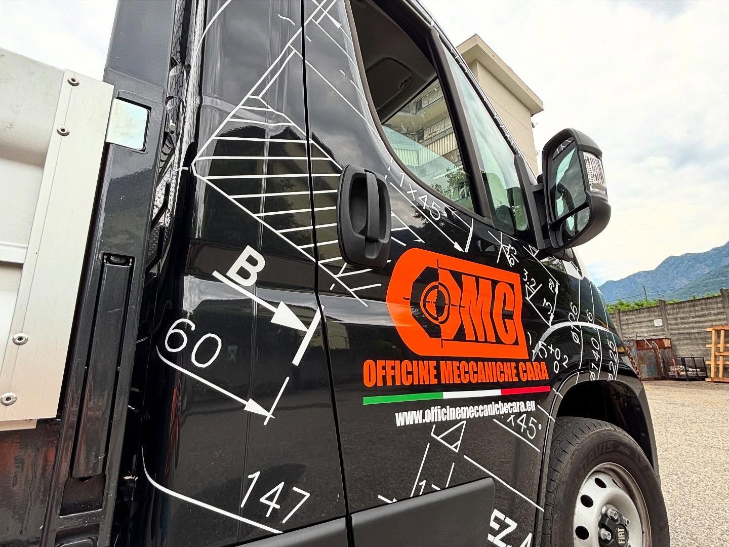 Uno sportello di camion nero con disegni tecnici, logo aziendale arancione e un dettaglio con la bandiera italiana.