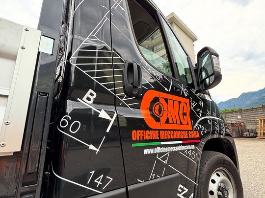 Uno sportello di camion nero con disegni tecnici, logo aziendale arancione e un dettaglio con la bandiera italiana.