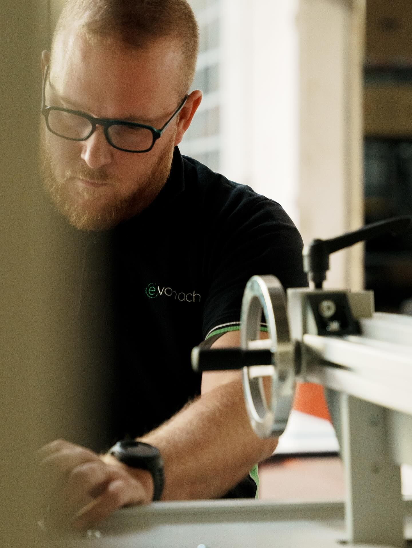 Una persona con gli occhiali e la barba è concentrata sull'utilizzo di una macchina manuale da officina.