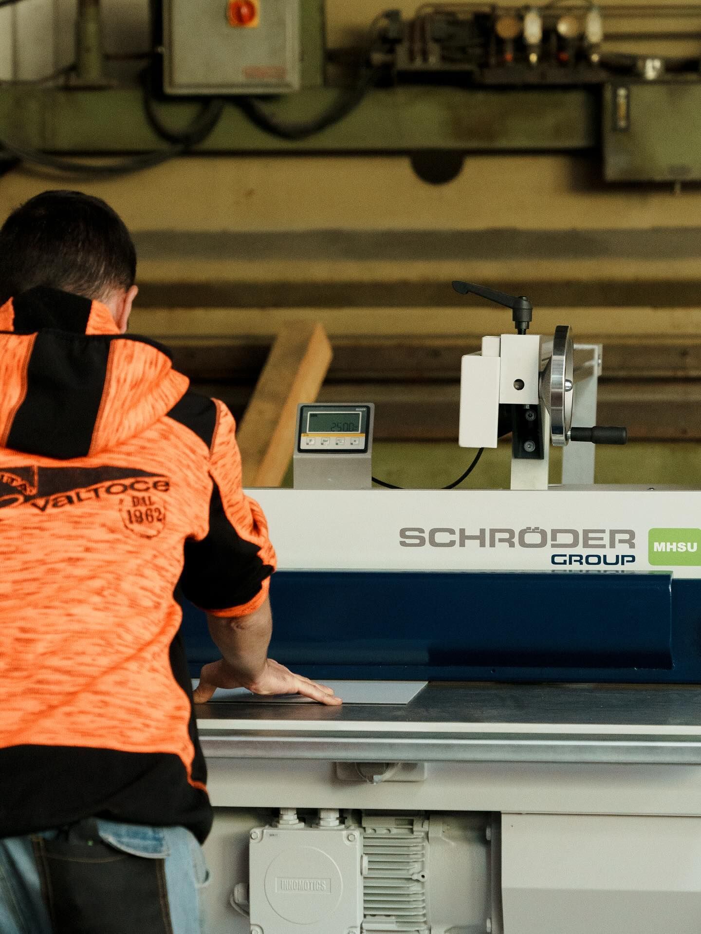 In un'officina, una persona con una felpa arancione e nera aziona una piegatrice per metalli industriale di marca Schroder.