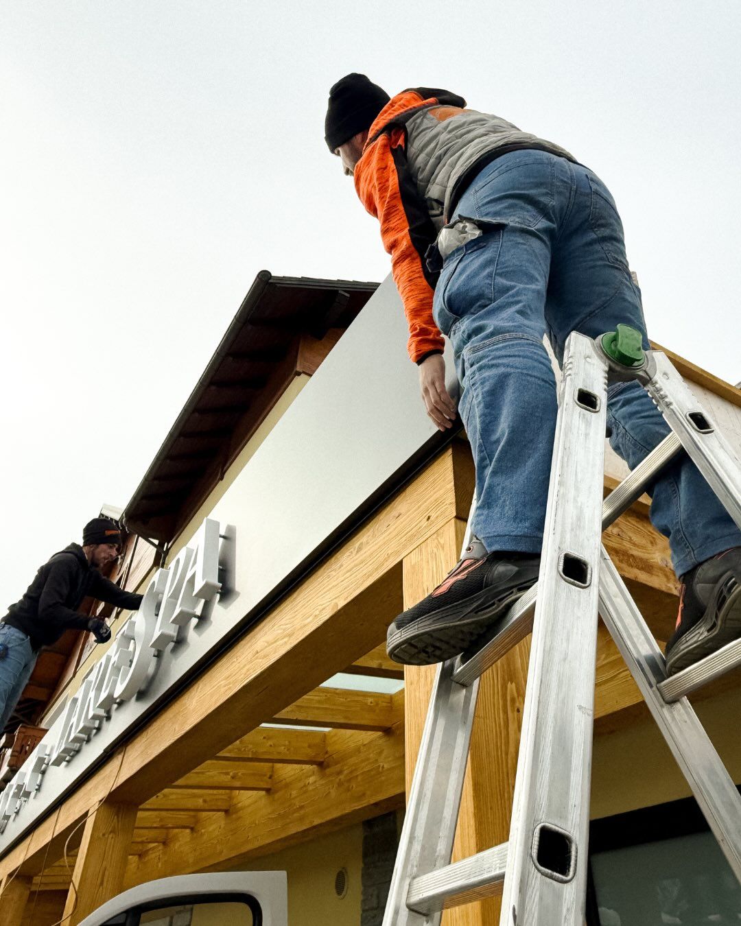 Due operai su una scala installano cartelli tridimensionali sulla struttura esterna in legno di un edificio.