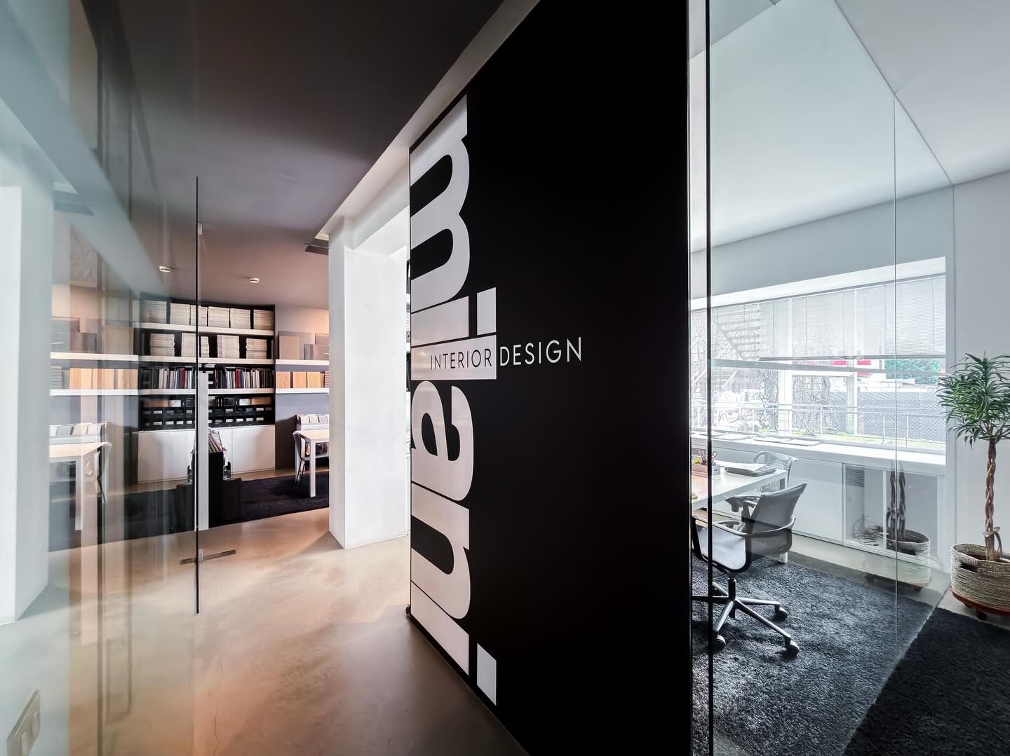 Interno di un ufficio moderno caratterizzato da un'ampia parete nera con testo bianco e divisori in vetro, visto da un corridoio.