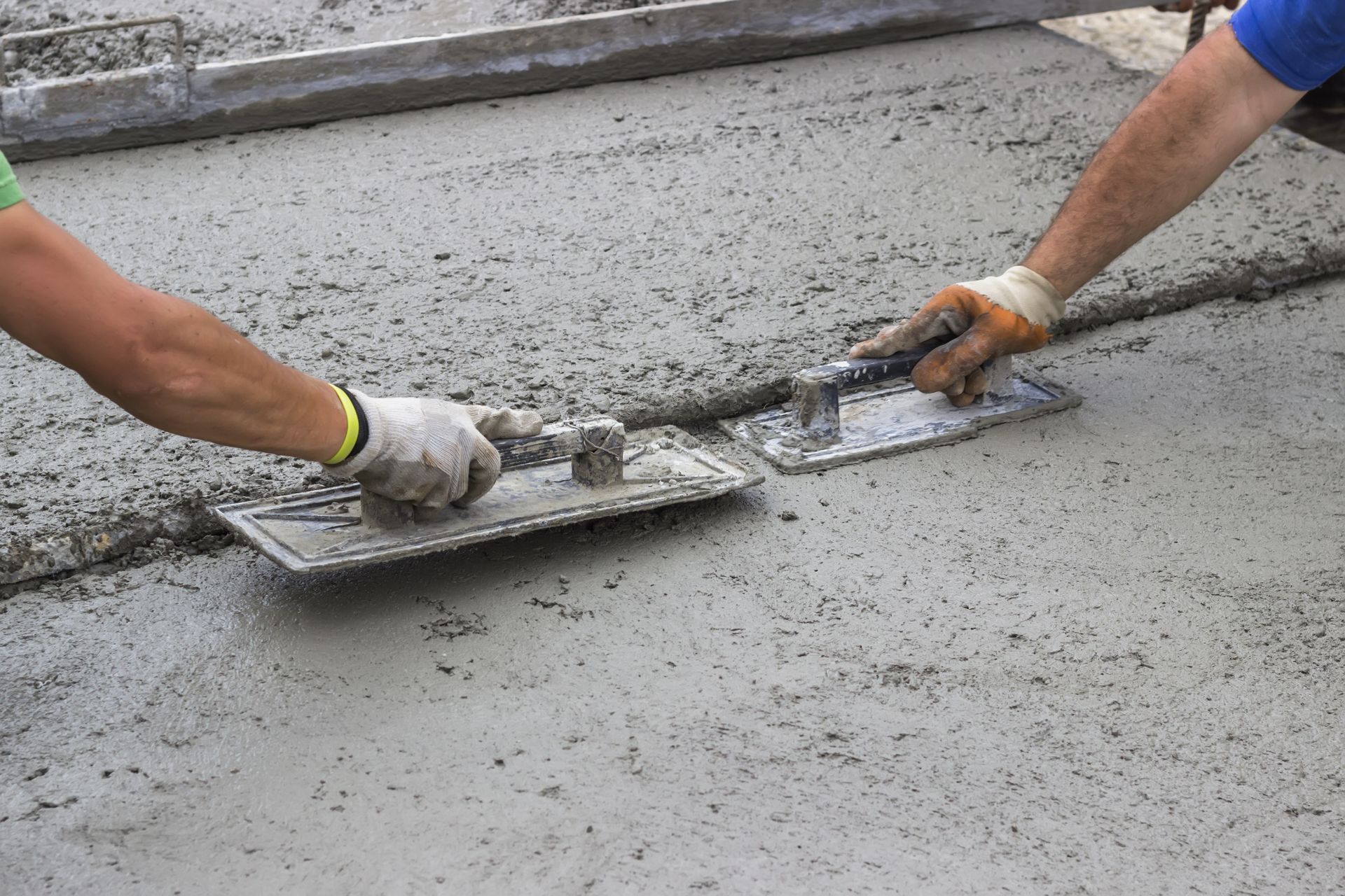 Leveling concrete with trowels, mason hands spreading poured concrete