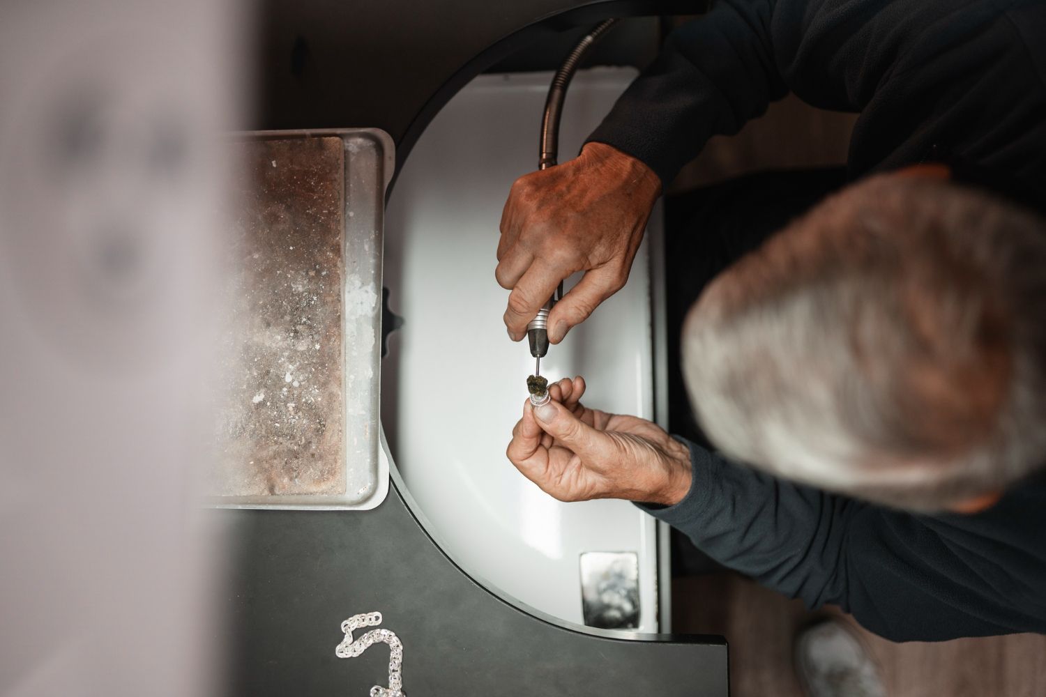 Person fixing jewelry with a tool by a sink, close-up overhead view.