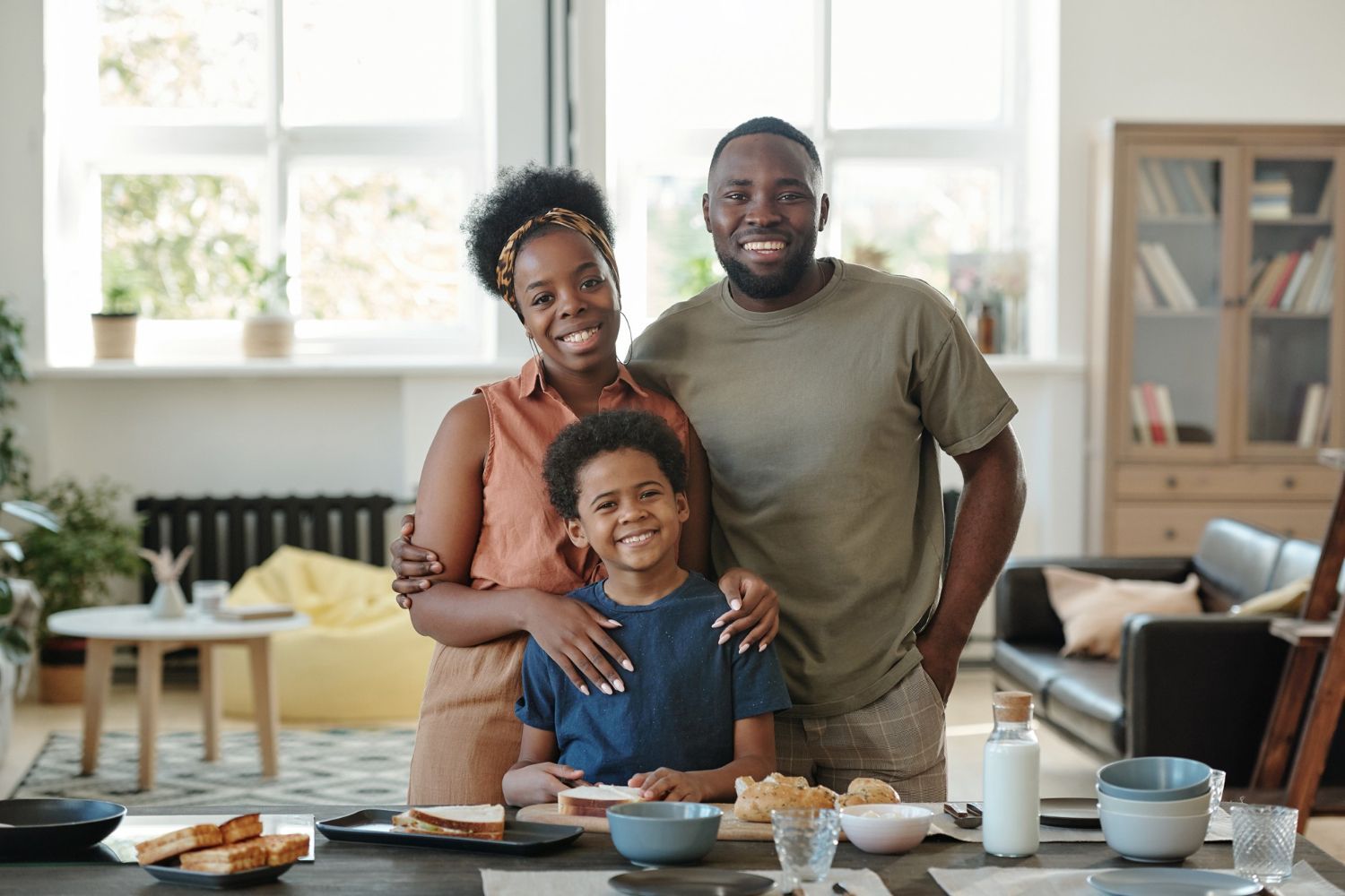 Family of three smiling together at a table in a home.