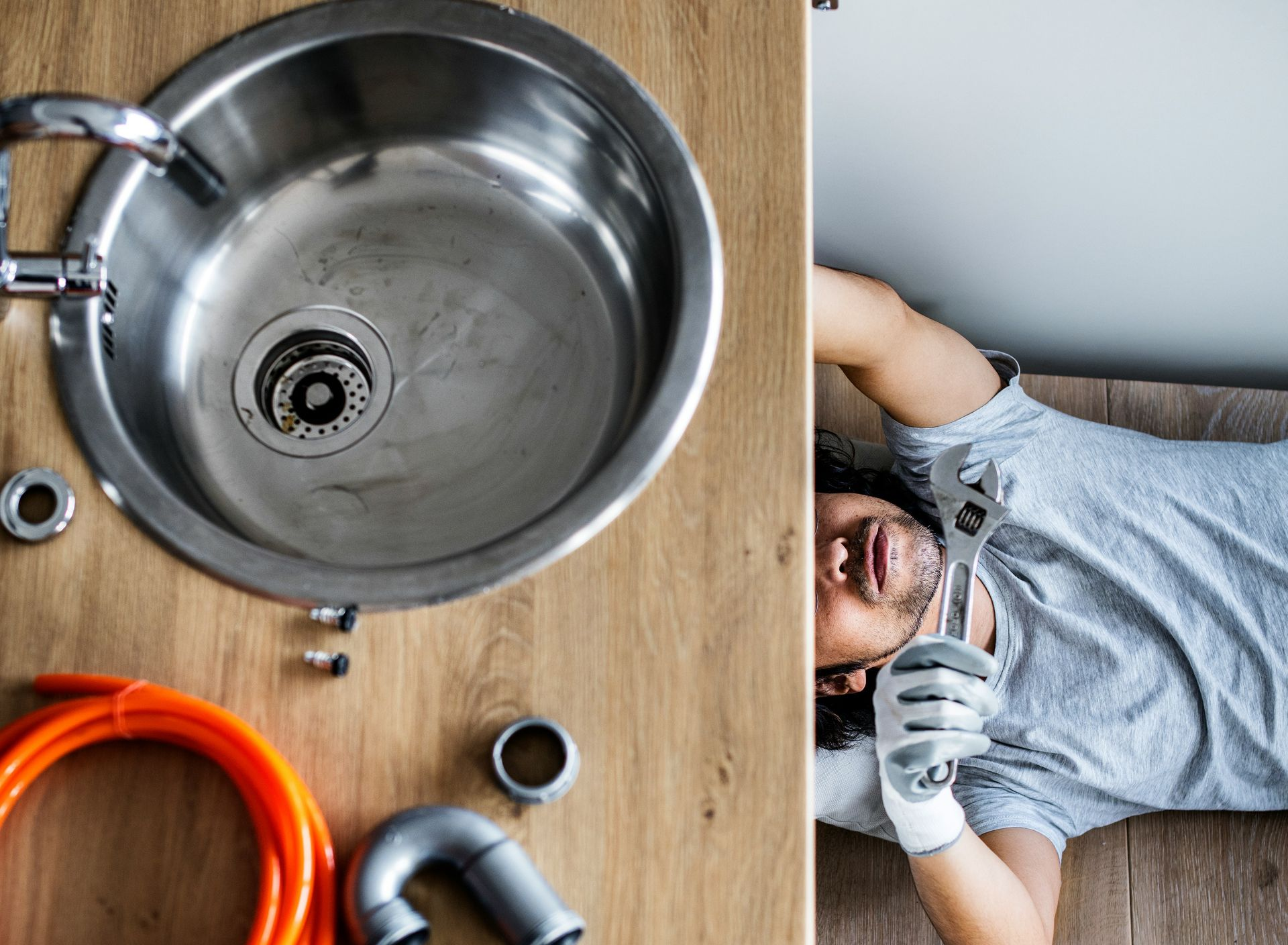 Plumber fixing a kitchen sink. View from above. Man is working under a sink with tools.