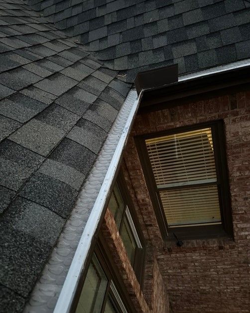 A gutter on the side of a brick building next to a window.