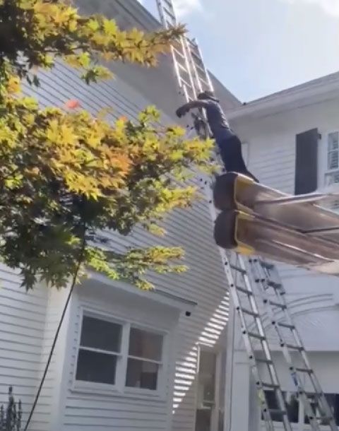 A man is standing on a ladder on the side of a house.