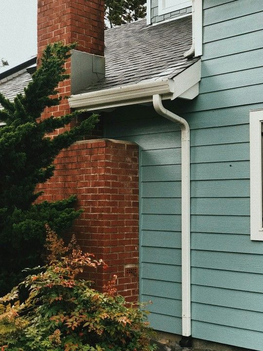 A blue house with a white gutter and a brick chimney