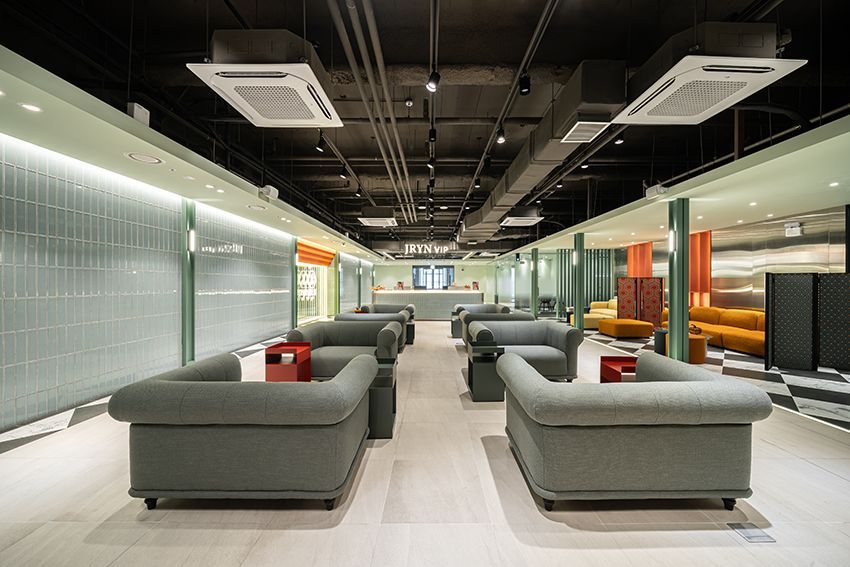 Modern lounge with gray sofas, glass walls, and orange accent chairs in a sleek office interior