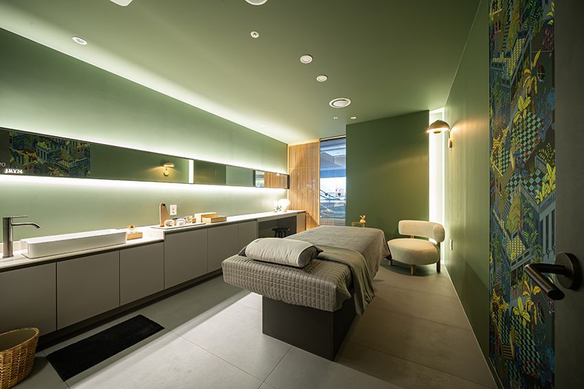 Modern spa treatment room with two massage beds, soft lighting, and green walls