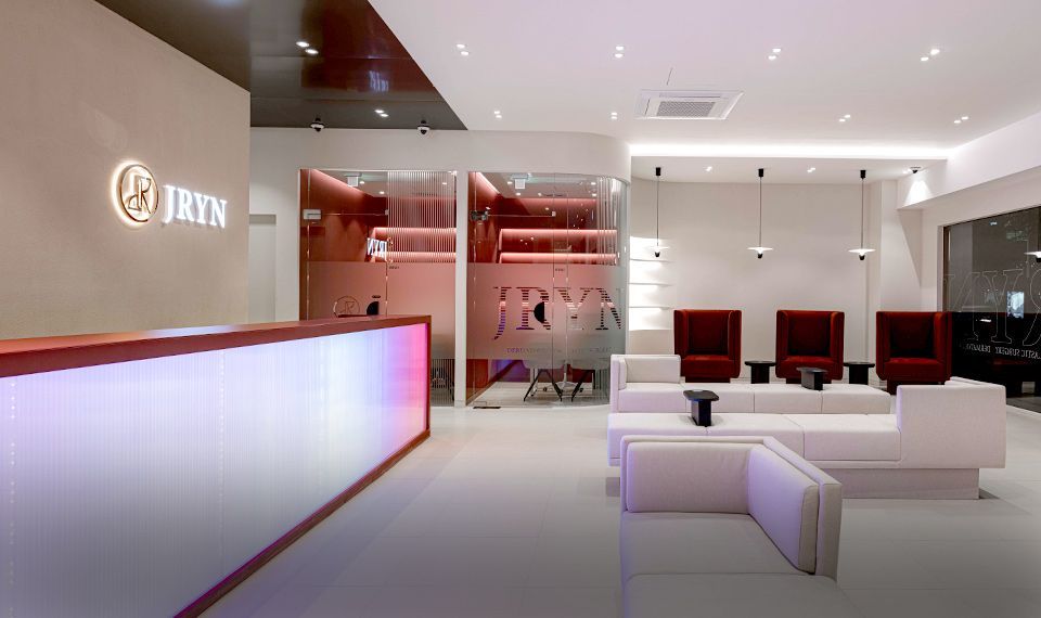 Modern minimalist lobby with a white reception desk, red seating, and soft pink lighting.
