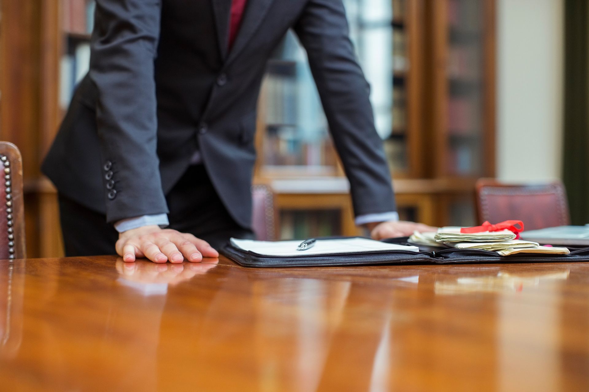A man in a suit and tie is leaning on a wooden table.