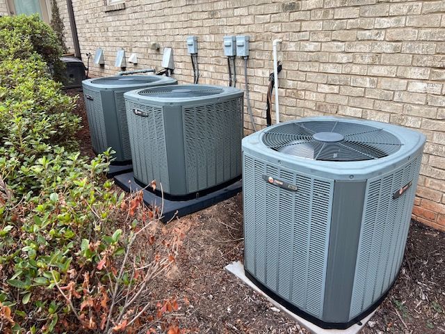 Two air conditioners are sitting next to each other in front of a brick wall.