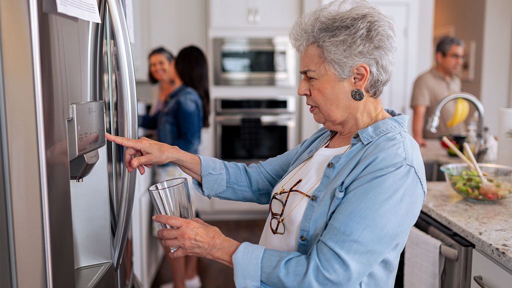 Women trying to fill her cup with water, but the refrigerator dispenser is 
not working
