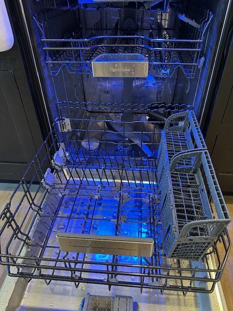The inside of a dishwasher with the door open and the lights on.